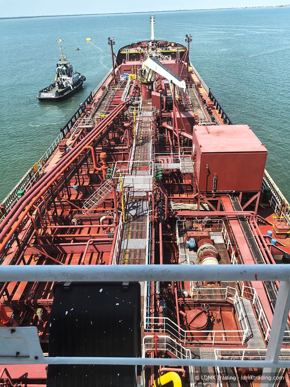 Bow of a product tanker at a CEMAC anchorage, with a tug alongside.