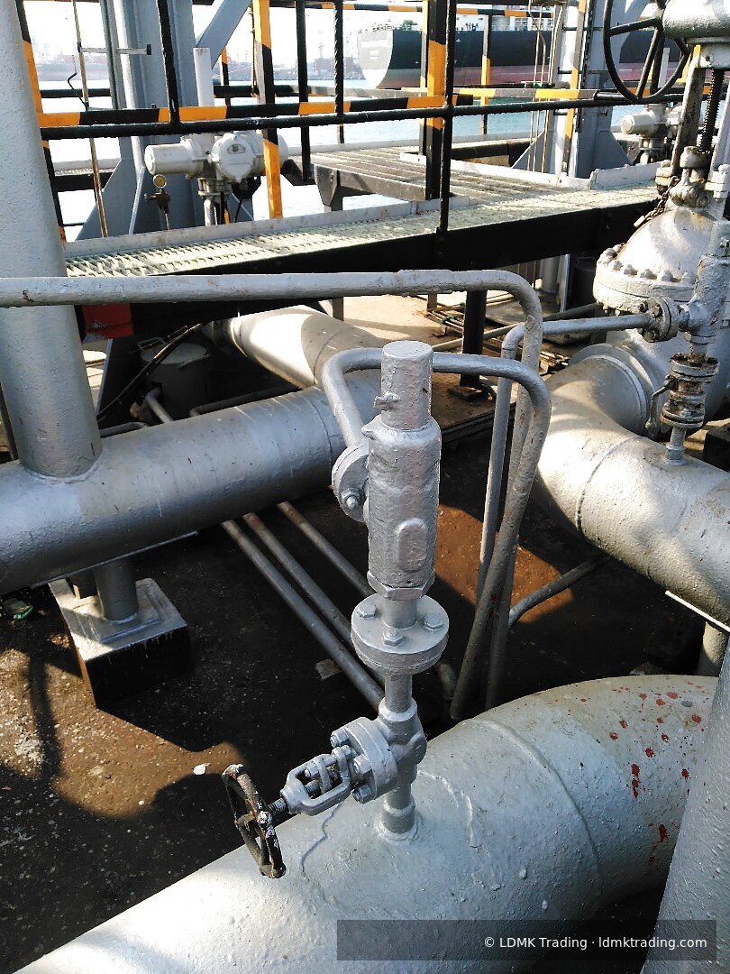 Painted valve and pipe manifold on a jetty with a tanker moored in the background.